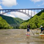 Paddle-boarders navigate toward New River Gorge Bridge