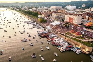 An aerial view shows the Charleston Sternwheel Regatta stretching along the Kanawha River as pleasure boats, historic sternwheelers, festival activities, and thousands of visitors fill the city's riverfront during the Independence Day weekend celebration.
