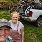 Krissy Stiver and Heather Stiver pose beside a pickup truck loaded with scrap metal collected during a community cleanup in Winona, W.Va. Volunteers removed abandoned metal, tires, and other debris as part of an effort that cleared nearly 7.7 tons of trash from the former coal community.