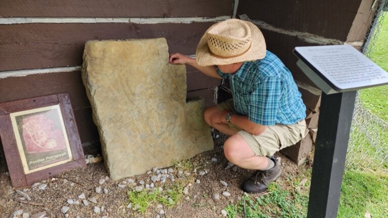 West Virginia Explorer publisher David Sibray examines the Water Panther Stone at Tu-Endie-Wei State Park in Point Pleasant, W.Va. The prehistoric petroglyph has been interpreted as depicting an Underwater Panther, a powerful being represented in Indigenous traditions and rock art.