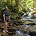 Filmmaker Emma Crow-Willard pauses beside a mountain stream while hiking West Virginia's 320-mile Allegheny Trail. Her month-long journey combines backpacking with interviews exploring the changing economies of communities along the route.