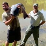 Tyler Harmon holds the 72.75-pound blue catfish he caught in the Ohio River in Jackson County as a West Virginia Division of Natural Resources official assists with the record certification. The fish set a new state weight record and was released alive. (WVDNR photo)