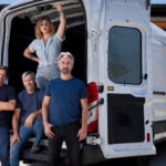 Four members of the American Pickers television production pose beside and inside a white Antique Archaeology van.