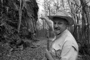 West Virginia Explorer publisher David Sibray points toward McKinley Rock along the former railroad corridor near Thurmond in the New River Gorge. According to local legend, the rock's resemblance to President William McKinley was interpreted as an omen of his assassination in 1901.