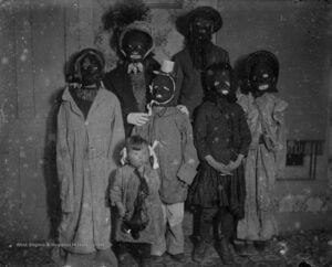 Historic black-and-white photograph of seven people, including children, wearing Halloween costumes and dark masks, circa 1900–1910.