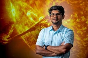 WVU aerospace engineering professor Piyush Mehta stands with arms crossed in front of an image of a solar eruption.