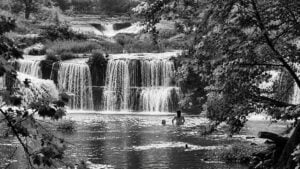 Swimmers enjoy the waters below Sandstone Falls on the New River in West Virginia. According to local ghost lore, a mysterious light associated with the spirit of Samuel Richmond, who was killed during the Civil War, is said to appear near the falls. The photograph has been converted to black and white.