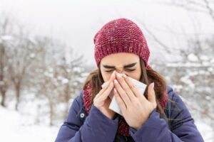 A woman uses a tissue while outdoors in winter. Health officials recommend annual influenza vaccinations and other preventive measures to reduce the spread of flu.